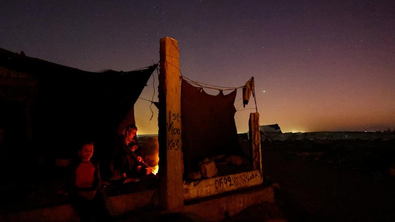 Warga Palestina yang mengungsi menyalakan api di tenda mereka saat mereka tinggal di pemakaman, di tengah konflik Israel-Hamas, di Khan Younis, di Jalur Gaza selatan, 27 Oktober 2024. (REUTERS/Mohammed Salem)