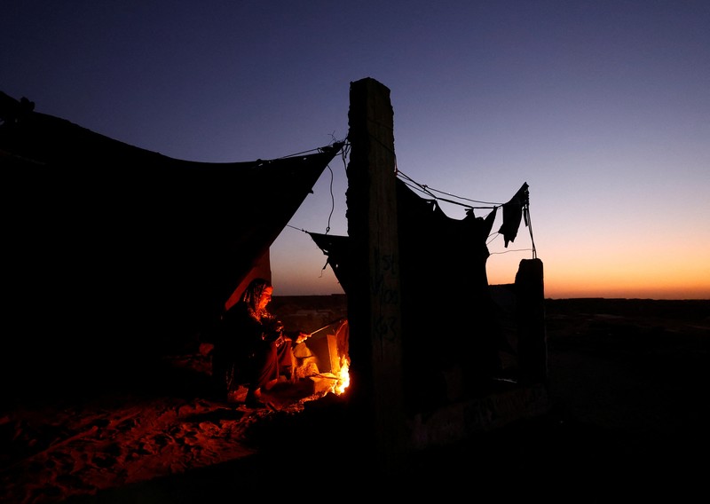 Warga Palestina yang mengungsi menyalakan api di tenda mereka saat mereka tinggal di pemakaman, di tengah konflik Israel-Hamas, di Khan Younis, di Jalur Gaza selatan, 27 Oktober 2024. (REUTERS/Mohammed Salem)