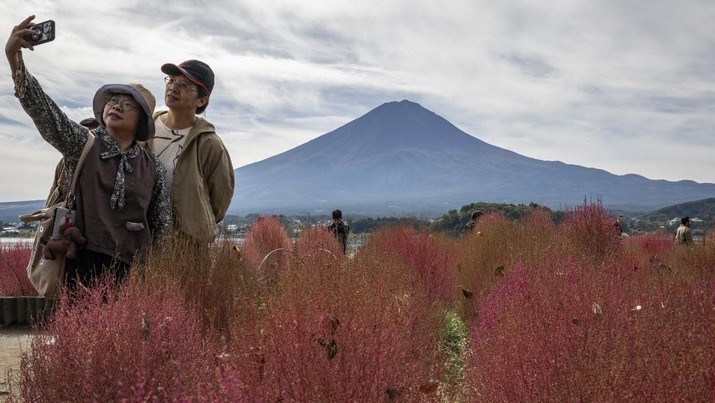 Warga beraktivitas dengan latar belakang Gunung Fuji, gunung tertinggi di Jepang dengan ketinggian 3.776 meter (12.460 kaki), di Fujikawaguchiko, prefektur Yamanashi pada tanggal 31 Oktober 2024. (AFP/YUICHI YAMAZAKI)