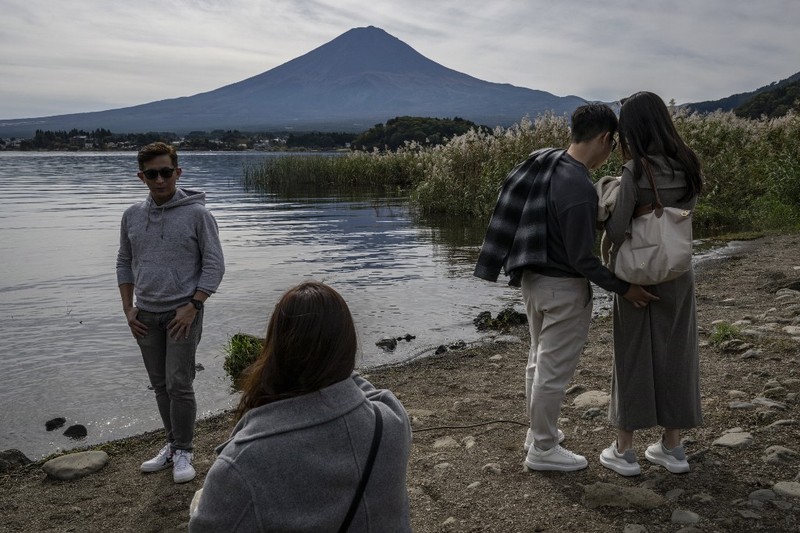 Warga beraktivitas dengan latar belakang Gunung Fuji, gunung tertinggi di Jepang dengan ketinggian 3.776 meter (12.460 kaki), di Fujikawaguchiko, prefektur Yamanashi pada tanggal 31 Oktober 2024. (AFP/YUICHI YAMAZAKI)