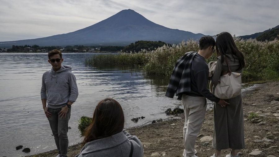 Warga beraktivitas dengan latar belakang Gunung Fuji, gunung tertinggi di Jepang dengan ketinggian 3.776 meter (12.460 kaki), di Fujikawaguchiko, prefektur Yamanashi pada tanggal 31 Oktober 2024. (AFP/YUICHI YAMAZAKI)