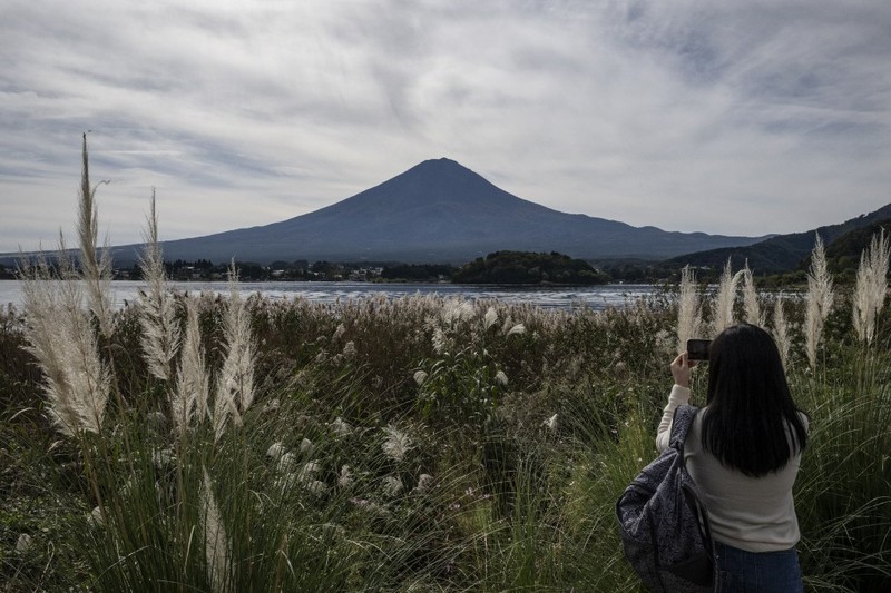 Warga beraktivitas dengan latar belakang Gunung Fuji, gunung tertinggi di Jepang dengan ketinggian 3.776 meter (12.460 kaki), di Fujikawaguchiko, prefektur Yamanashi pada tanggal 31 Oktober 2024. (AFP/YUICHI YAMAZAKI)