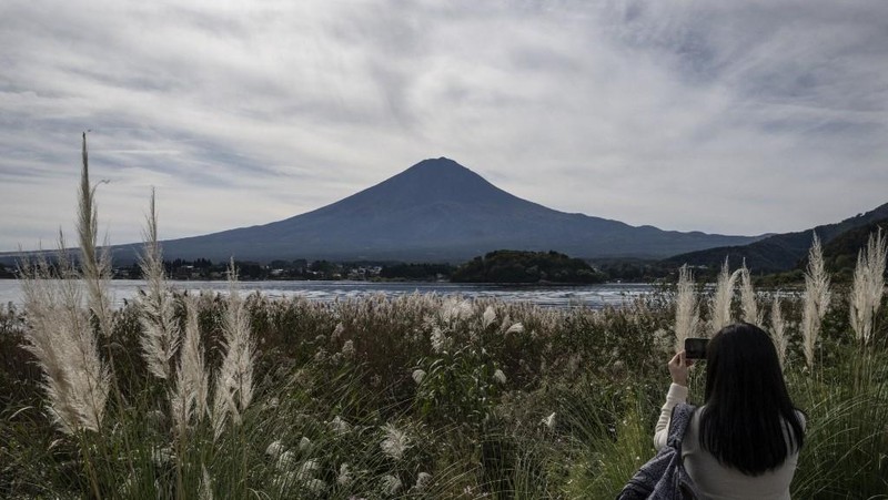 Warga beraktivitas dengan latar belakang Gunung Fuji, gunung tertinggi di Jepang dengan ketinggian 3.776 meter (12.460 kaki), di Fujikawaguchiko, prefektur Yamanashi pada tanggal 31 Oktober 2024. (AFP/YUICHI YAMAZAKI)