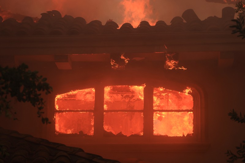 Pemandangan menunjukkan properti yang rusak terbakar, sementara asap mengepul dari Kebakaran Gunung di Camarillo, California, AS, 6 November 2024. (REUTERS/David Swanson)