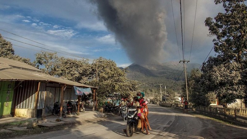 Warga berkendara dengan latar belakang Gunung Lewotobi Laki Laki memuntahkan material vulkanik saat terjadi letusan di Flores Timur, Indonesia, Sabtu, 9 November 2024.(Photo by ARNOLD WELIANTO / AFP)