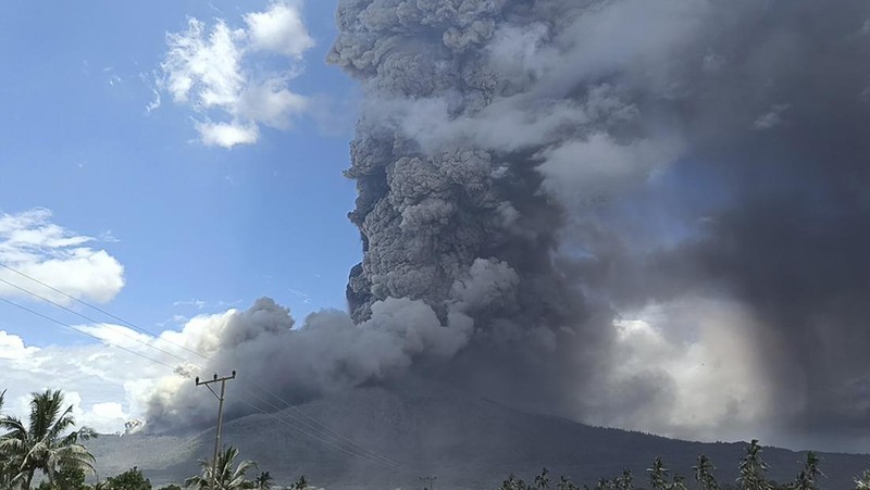 Warga berkendara dengan latar belakang Gunung Lewotobi Laki Laki memuntahkan material vulkanik saat terjadi letusan di Flores Timur, Indonesia, Sabtu, 9 November 2024.(Photo by ARNOLD WELIANTO / AFP)