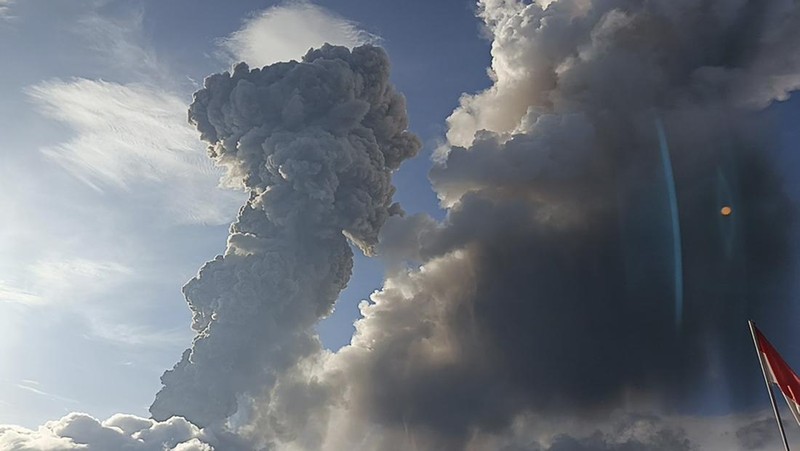 Warga berkendara dengan latar belakang Gunung Lewotobi Laki Laki memuntahkan material vulkanik saat terjadi letusan di Flores Timur, Indonesia, Sabtu, 9 November 2024.(Photo by ARNOLD WELIANTO / AFP)