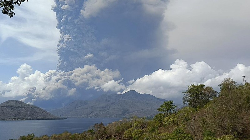 Warga berkendara dengan latar belakang Gunung Lewotobi Laki Laki memuntahkan material vulkanik saat terjadi letusan di Flores Timur, Indonesia, Sabtu, 9 November 2024.(Photo by ARNOLD WELIANTO / AFP)