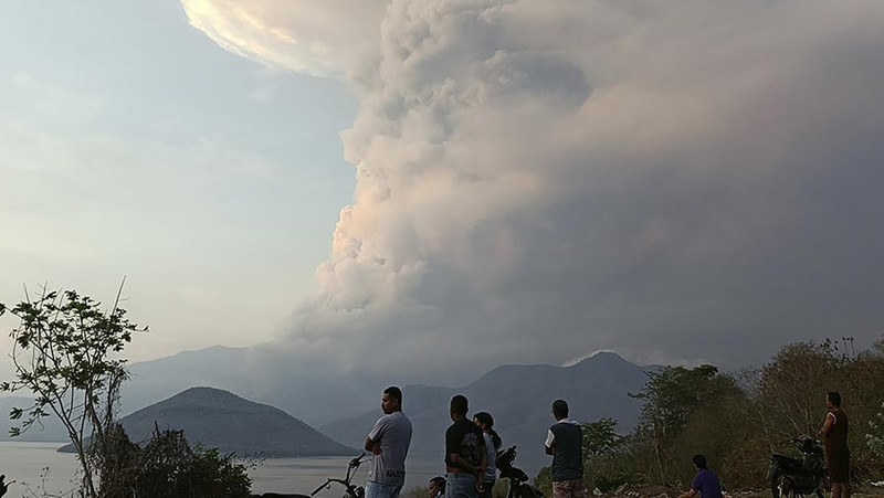 Warga berkendara dengan latar belakang Gunung Lewotobi Laki Laki memuntahkan material vulkanik saat terjadi letusan di Flores Timur, Indonesia, Sabtu, 9 November 2024.(Photo by ARNOLD WELIANTO / AFP)