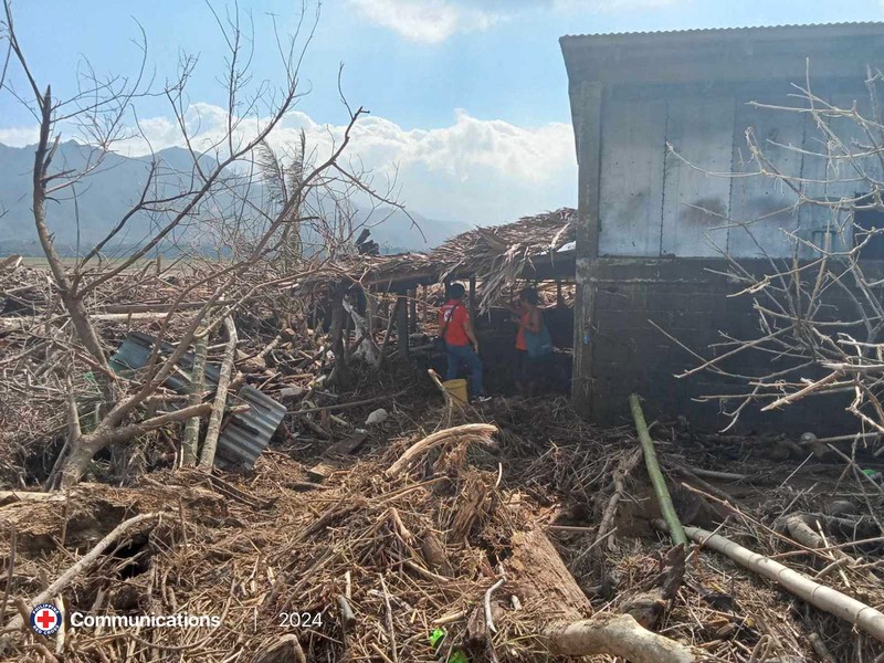 Warga berjalan di atas kayu gelondongan dan puing-puing yang tersapu banjir akibat Topan Usagi di Gonzaga, provinsi Cagayan, Filipina utara, Jumat (15/11/2024). (AP Photo/Noel Celis)