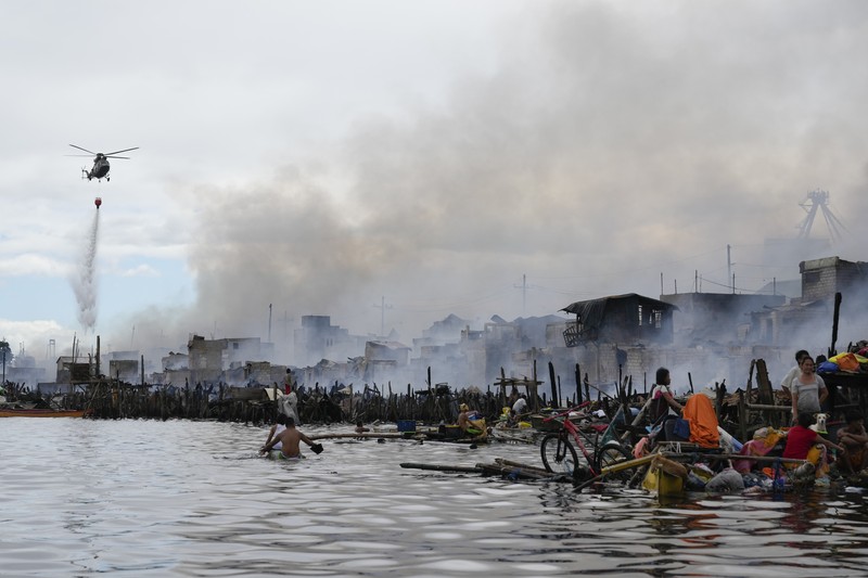 Philippines Fire A Philippine Air Force helicopter drops water on burning homes as fire broke out at a slum area leaving about 2,000 families homeless on Sunday, Nov. 24, 2024 in Manila, Philippines. (AP Photo/Aaron Favila)