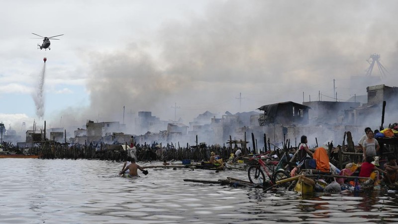 A Philippine Air Force helicopter drops water on burning homes as fire broke out at a slum area leaving about 2,000 families homeless on Sunday, Nov. 24, 2024 in Manila, Philippines. (AP Photo/Aaron Favila)