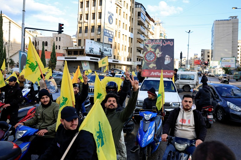 Seseorang memberi isyarat sambil memegang poster bergambar mendiang pemimpin Hizbullah Sayyed Hassan Nasrallah, di pintu masuk pinggiran selatan Beirut, setelah gencatan senjata antara Israel dan kelompok Hizbullah yang didukung Iran mulai berlaku pada pukul 02.00 GMT pada hari Rabu setelah Presiden AS Joe Biden mengatakan kedua belah pihak menerima perjanjian yang ditengahi oleh Amerika Serikat dan Prancis, di Lebanon, 27 November 2024. (REUTERS/Thaier Al-Sudani)
