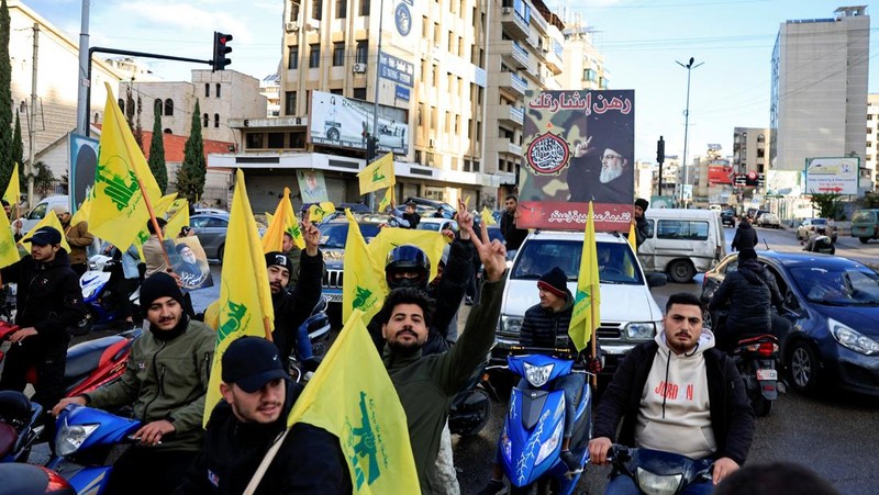 Seseorang memberi isyarat sambil memegang poster bergambar mendiang pemimpin Hizbullah Sayyed Hassan Nasrallah, di pintu masuk pinggiran selatan Beirut, setelah gencatan senjata antara Israel dan kelompok Hizbullah yang didukung Iran mulai berlaku pada pukul 02.00 GMT pada hari Rabu setelah Presiden AS Joe Biden mengatakan kedua belah pihak menerima perjanjian yang ditengahi oleh Amerika Serikat dan Prancis, di Lebanon, 27 November 2024. (REUTERS/Thaier Al-Sudani)