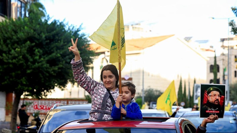 Seseorang memberi isyarat sambil memegang poster bergambar mendiang pemimpin Hizbullah Sayyed Hassan Nasrallah, di pintu masuk pinggiran selatan Beirut, setelah gencatan senjata antara Israel dan kelompok Hizbullah yang didukung Iran mulai berlaku pada pukul 02.00 GMT pada hari Rabu setelah Presiden AS Joe Biden mengatakan kedua belah pihak menerima perjanjian yang ditengahi oleh Amerika Serikat dan Prancis, di Lebanon, 27 November 2024. (REUTERS/Thaier Al-Sudani)