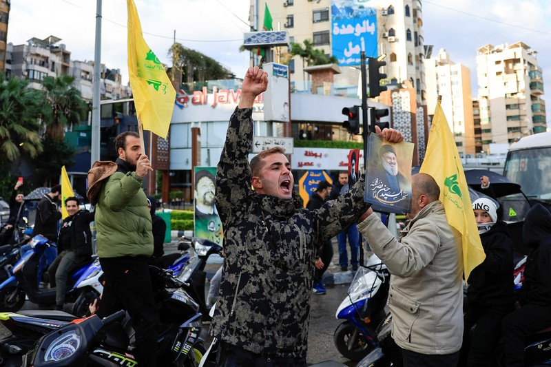 Seseorang memberi isyarat sambil memegang poster bergambar mendiang pemimpin Hizbullah Sayyed Hassan Nasrallah, di pintu masuk pinggiran selatan Beirut, setelah gencatan senjata antara Israel dan kelompok Hizbullah yang didukung Iran mulai berlaku pada pukul 02.00 GMT pada hari Rabu setelah Presiden AS Joe Biden mengatakan kedua belah pihak menerima perjanjian yang ditengahi oleh Amerika Serikat dan Prancis, di Lebanon, 27 November 2024. Seseorang memberi isyarat sambil memegang poster bergambar mendiang pemimpin Hizbullah Sayyed Hassan Nasrallah, di pintu masuk pinggiran selatan Beirut, setelah gencatan senjata antara Israel dan kelompok Hizbullah yang didukung Iran mulai berlaku pada pukul 02.00 GMT pada hari Rabu setelah Presiden AS Joe Biden mengatakan kedua belah pihak menerima perjanjian yang ditengahi oleh Amerika Serikat dan Prancis, di Lebanon, 27 November 2024. (REUTERS/Thaier Al-Sudani)