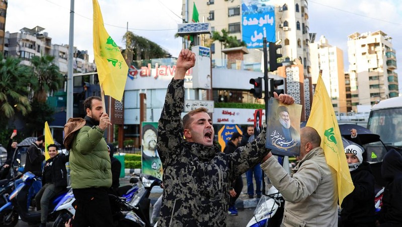 Seseorang memberi isyarat sambil memegang poster bergambar mendiang pemimpin Hizbullah Sayyed Hassan Nasrallah, di pintu masuk pinggiran selatan Beirut, setelah gencatan senjata antara Israel dan kelompok Hizbullah yang didukung Iran mulai berlaku pada pukul 02.00 GMT pada hari Rabu setelah Presiden AS Joe Biden mengatakan kedua belah pihak menerima perjanjian yang ditengahi oleh Amerika Serikat dan Prancis, di Lebanon, 27 November 2024. (REUTERS/Thaier Al-Sudani)