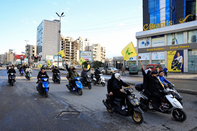 Men carry Hezbollah flags and a picture depicting late Hezbollah leader Sayyed Hassan Nasrallah, as they drive past damaged buildings at the entrance of Beirut's southern suburbs, after a ceasefire between Israel and Hezbollah took effect, Lebanon November 27, 2024. REUTERS/Mohamed Azakir     TPX IMAGES OF THE DAY