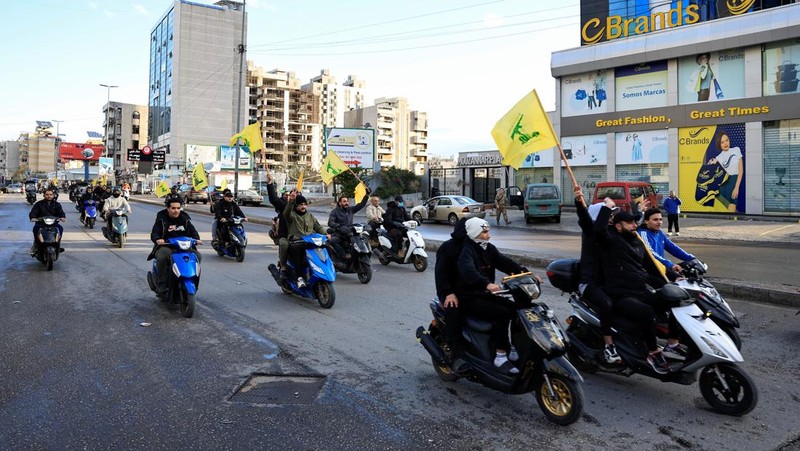 Men carry Hezbollah flags and a picture depicting late Hezbollah leader Sayyed Hassan Nasrallah, as they drive past damaged buildings at the entrance of Beirut's southern suburbs, after a ceasefire between Israel and Hezbollah took effect, Lebanon November 27, 2024. REUTERS/Mohamed Azakir     TPX IMAGES OF THE DAY