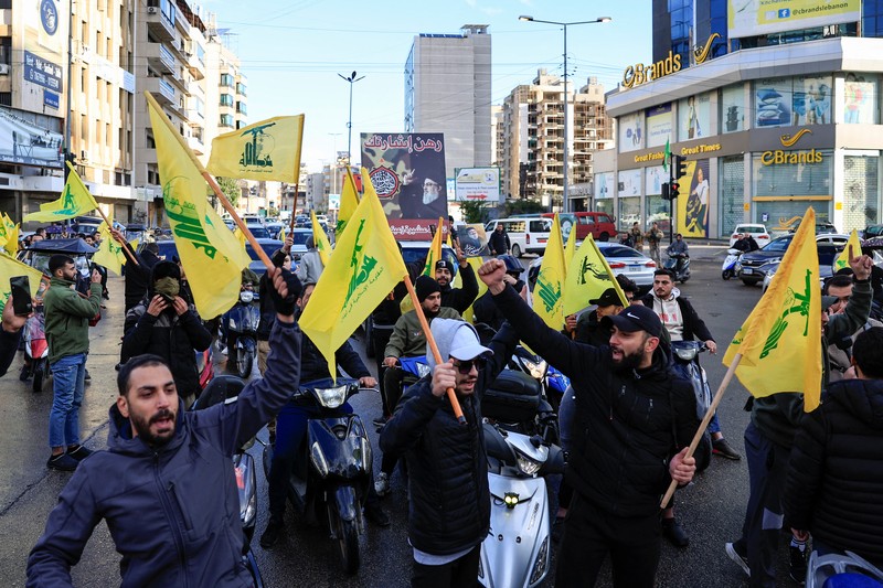 Men carry Hezbollah flags and a picture depicting late Hezbollah leader Sayyed Hassan Nasrallah, as they drive past damaged buildings at the entrance of Beirut's southern suburbs, after a ceasefire between Israel and Hezbollah took effect, Lebanon November 27, 2024. REUTERS/Mohamed Azakir     TPX IMAGES OF THE DAY