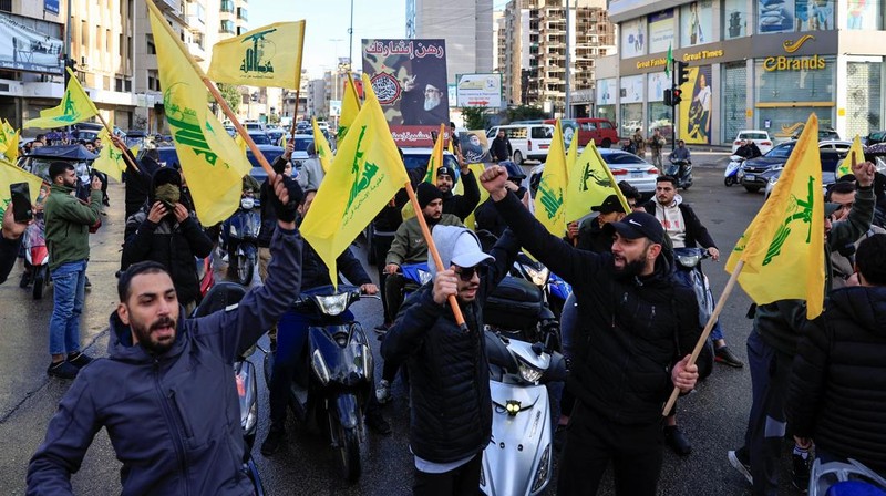 Men carry Hezbollah flags and a picture depicting late Hezbollah leader Sayyed Hassan Nasrallah, as they drive past damaged buildings at the entrance of Beirut's southern suburbs, after a ceasefire between Israel and Hezbollah took effect, Lebanon November 27, 2024. REUTERS/Mohamed Azakir     TPX IMAGES OF THE DAY