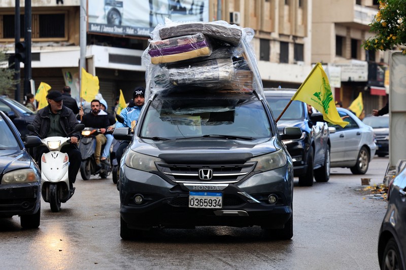 Men carry Hezbollah flags and a picture depicting late Hezbollah leader Sayyed Hassan Nasrallah, as they drive past damaged buildings at the entrance of Beirut's southern suburbs, after a ceasefire between Israel and Hezbollah took effect, Lebanon November 27, 2024. REUTERS/Mohamed Azakir     TPX IMAGES OF THE DAY