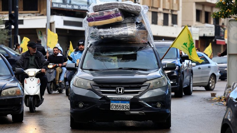 Men carry Hezbollah flags and a picture depicting late Hezbollah leader Sayyed Hassan Nasrallah, as they drive past damaged buildings at the entrance of Beirut's southern suburbs, after a ceasefire between Israel and Hezbollah took effect, Lebanon November 27, 2024. REUTERS/Mohamed Azakir     TPX IMAGES OF THE DAY