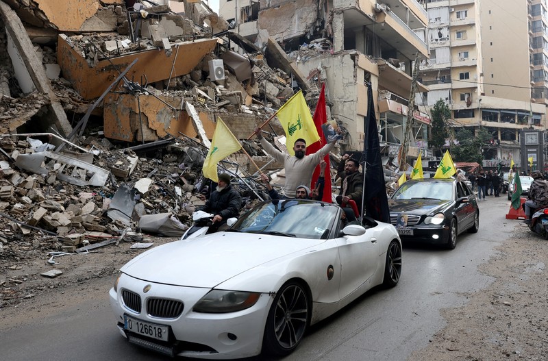 Men carry Hezbollah flags and a picture depicting late Hezbollah leader Sayyed Hassan Nasrallah, as they drive past damaged buildings at the entrance of Beirut's southern suburbs, after a ceasefire between Israel and Hezbollah took effect, Lebanon November 27, 2024. REUTERS/Mohamed Azakir     TPX IMAGES OF THE DAY