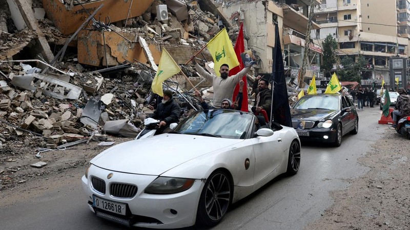 Men carry Hezbollah flags and a picture depicting late Hezbollah leader Sayyed Hassan Nasrallah, as they drive past damaged buildings at the entrance of Beirut's southern suburbs, after a ceasefire between Israel and Hezbollah took effect, Lebanon November 27, 2024. REUTERS/Mohamed Azakir     TPX IMAGES OF THE DAY