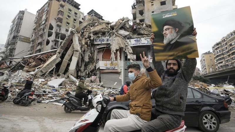 Men carry Hezbollah flags and a picture depicting late Hezbollah leader Sayyed Hassan Nasrallah, as they drive past damaged buildings at the entrance of Beirut's southern suburbs, after a ceasefire between Israel and Hezbollah took effect, Lebanon November 27, 2024. REUTERS/Mohamed Azakir     TPX IMAGES OF THE DAY