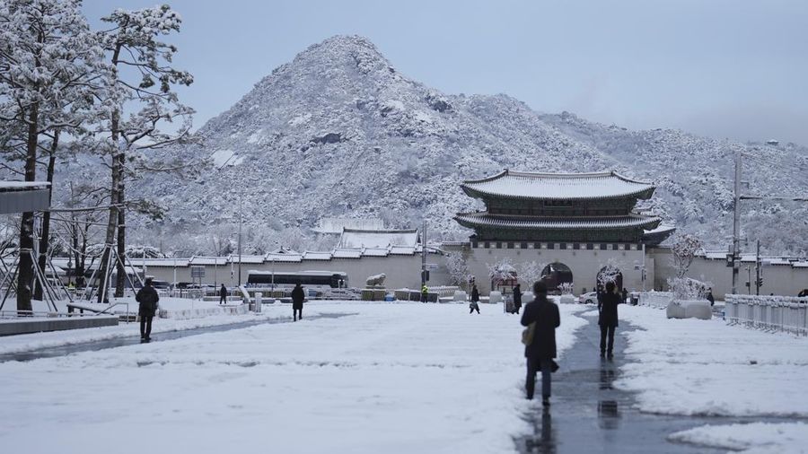Pedestrians stop to take photos of the snow-covered Gwanghwamun, the main gate of the 14th-century Gyeongbok Palace, one of South Korea's well known landmarks, in Seoul, South Korea, Wednesday, Nov. 27, 2024. (AP Photo/Lee Jin-man)