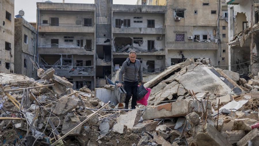 Samir Kassab, 53, membawa barang-barangnya saat berjalan di atas reruntuhan rumahnya yang hancur akibat serangan Israel, setelah gencatan senjata antara Israel dan Hizbullah, di Tyre, Lebanon selatan, 29 November 2024. (REUTERS/Adnan Abidi)