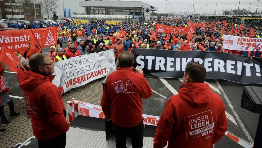Para pekerja pabrikan mobil asal Jerman, Volkswagen (VW) melakukan membawa bendera saat mereka melakukan mogok kerja di Hanover, Jerman, Senin (2/12/2024). (Jens Schlueter / AFP)
