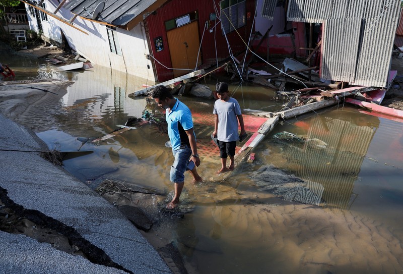 Orang-orang berjalan di atas bangunan rumah yang runtuh akibat banjir di Tumpat, Malaysia, pada tanggal 2 Desember 2024. (REUTERS/Hasnoor Hussain)