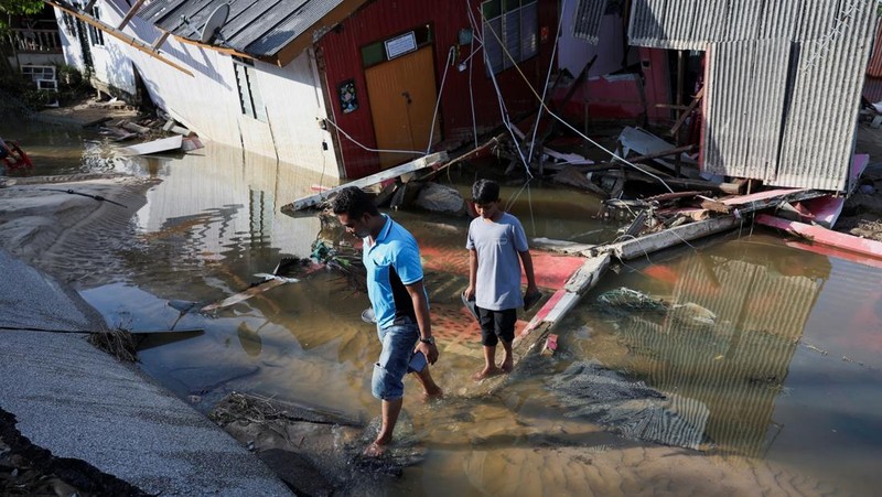 Orang-orang berjalan di atas bangunan rumah yang runtuh akibat banjir di Tumpat, Malaysia, pada tanggal 2 Desember 2024. (REUTERS/Hasnoor Hussain)