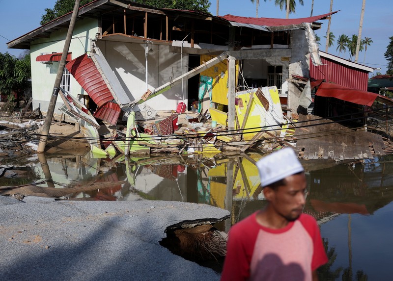 Orang-orang berjalan di atas bangunan rumah yang runtuh akibat banjir di Tumpat, Malaysia, pada tanggal 2 Desember 2024. (REUTERS/Hasnoor Hussain)