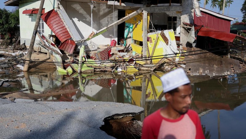 Orang-orang berjalan di atas bangunan rumah yang runtuh akibat banjir di Tumpat, Malaysia, pada tanggal 2 Desember 2024. (REUTERS/Hasnoor Hussain)