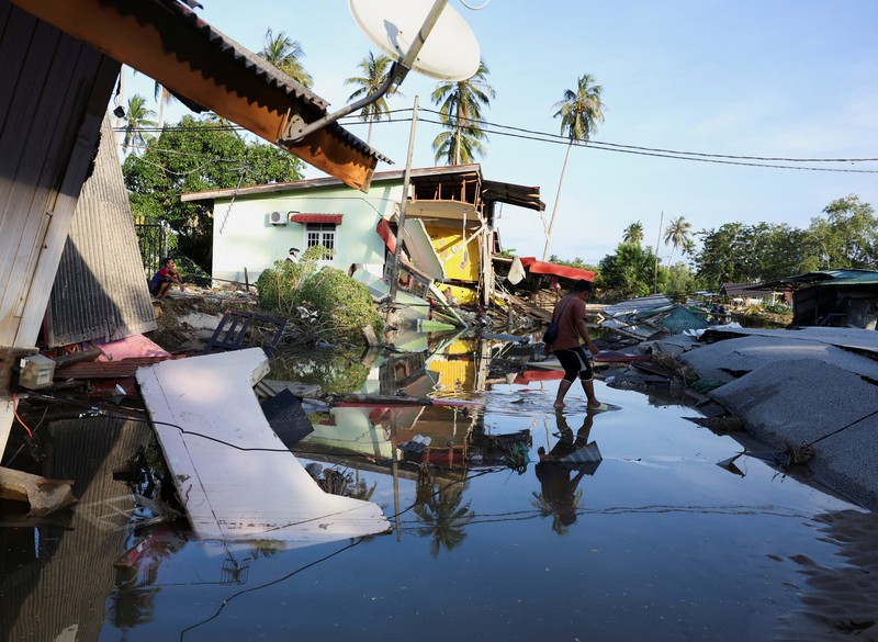 Orang-orang berjalan di atas bangunan rumah yang runtuh akibat banjir di Tumpat, Malaysia, pada tanggal 2 Desember 2024. (REUTERS/Hasnoor Hussain)