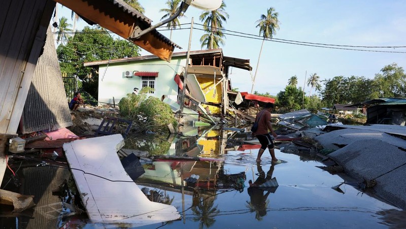 Orang-orang berjalan di atas bangunan rumah yang runtuh akibat banjir di Tumpat, Malaysia, pada tanggal 2 Desember 2024. (REUTERS/Hasnoor Hussain)