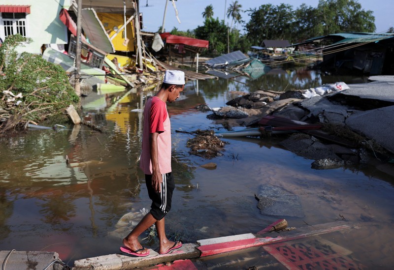 Orang-orang berjalan di atas bangunan rumah yang runtuh akibat banjir di Tumpat, Malaysia, pada tanggal 2 Desember 2024. (REUTERS/Hasnoor Hussain)