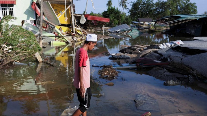 Orang-orang berjalan di atas bangunan rumah yang runtuh akibat banjir di Tumpat, Malaysia, pada tanggal 2 Desember 2024. (REUTERS/Hasnoor Hussain)