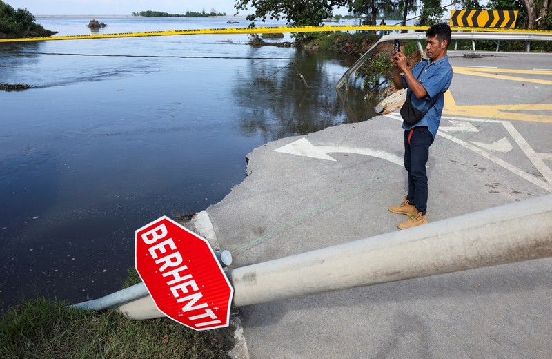 Orang-orang berjalan di atas bangunan rumah yang runtuh akibat banjir di Tumpat, Malaysia, pada tanggal 2 Desember 2024. (REUTERS/Hasnoor Hussain)