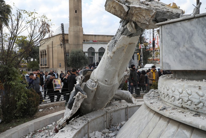 Orang-orang berdiri di dekat patung mantan presiden Suriah Hafez al-Assad yang rusak setelah pemberontak Suriah mengumumkan bahwa mereka telah menggulingkan Presiden Bashar al-Assad, di Qamishli, Suriah, 8 Desember 2024. (REUTERS/Orhan Qereman)