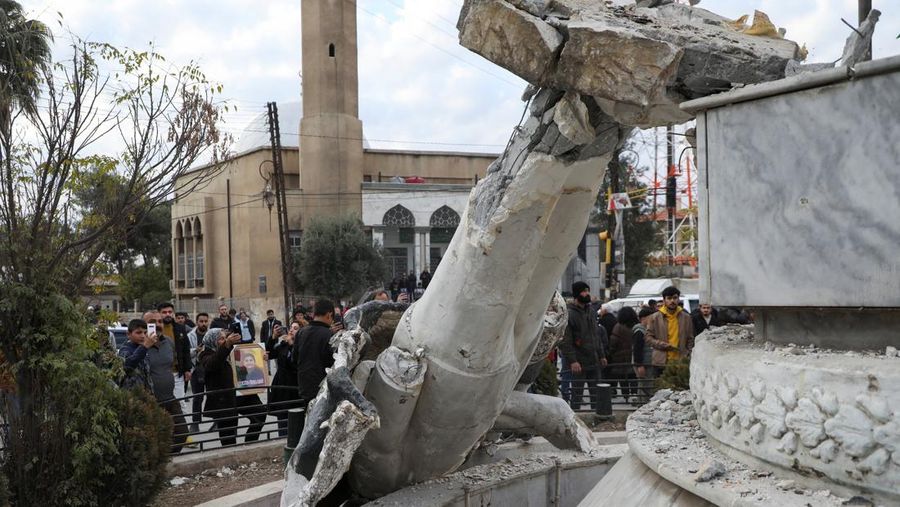 Orang-orang berdiri di dekat patung mantan presiden Suriah Hafez al-Assad yang rusak setelah pemberontak Suriah mengumumkan bahwa mereka telah menggulingkan Presiden Bashar al-Assad, di Qamishli, Suriah, 8 Desember 2024. (REUTERS/Orhan Qereman)