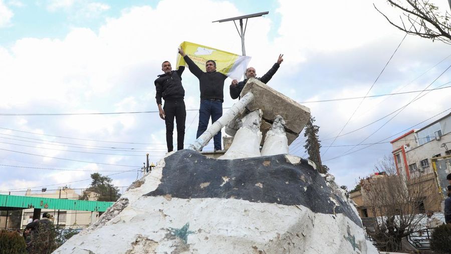 Orang-orang memberi isyarat sambil memegang bendera, setelah pemberontak Suriah mengumumkan bahwa mereka telah menggulingkan Presiden Bashar al-Assad, di Qamishli, Suriah, 8 Desember 2024. (REUTERS/Orhan Qereman)