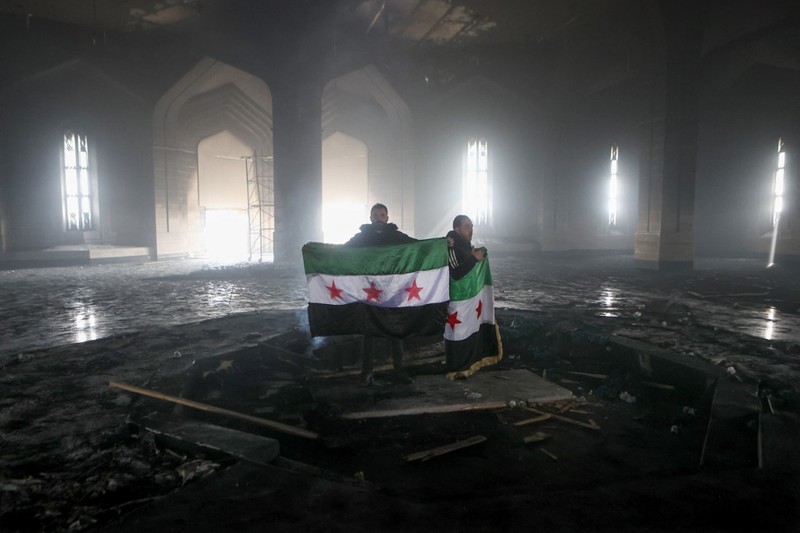 Kombinasi visual yang dibuat pada (11/12/2024) ini menunjukkan gambar (atas) yang diambil pada hari yang sama dari pejuang pemberontak yang berdiri dengan bendera oposisi di makam mendiang presiden Suriah Hafez al-Assad yang terbakar di makamnya di desa leluhur keluarga Qardaha di provinsi Latakia barat, setelah diserbu oleh faksi anti-Assad dan dibakar dan gambar arsip lain yang dirilis oleh Kantor Berita Arab Suriah (SANA) pada (16/11/2011) dari warga Suriah yang mengunjungi makam yang sama untuk memperingati ulang tahun Kombinasi visual yang dibuat pada (11/12/2024) ini menunjukkan gambar (atas) yang diambil pada hari yang sama dari pejuang pemberontak yang berdiri dengan bendera oposisi di makam mendiang presiden Suriah Hafez al-Assad yang terbakar di makamnya di desa leluhur keluarga Qardaha di provinsi Latakia barat, setelah diserbu oleh faksi anti-Assad dan dibakar dan gambar arsip lain yang dirilis oleh Kantor Berita Arab Suriah (SANA) pada (16/11/2011) dari warga Suriah yang mengunjungi makam yang sama untuk memperingati ulang tahun