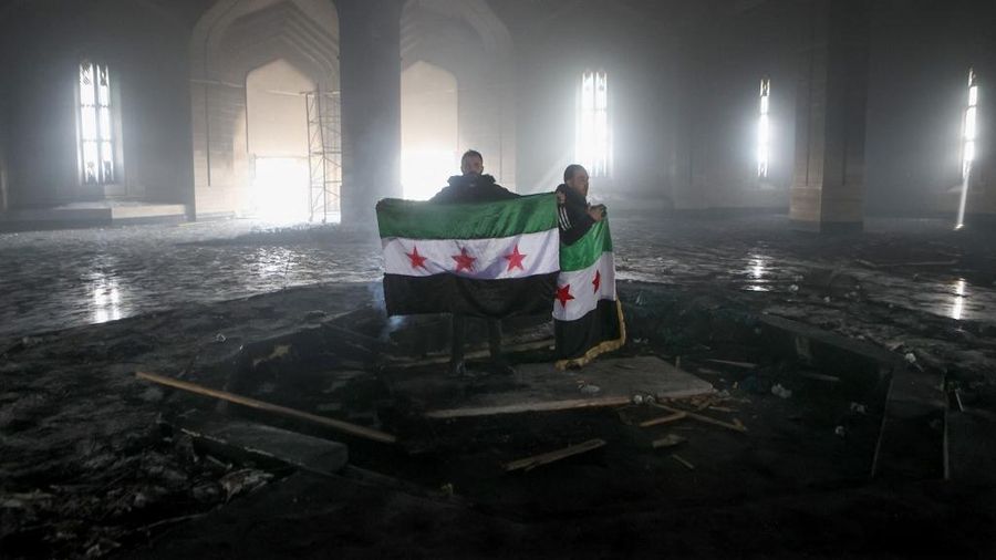 Kombinasi visual yang dibuat pada (11/12/2024) ini menunjukkan gambar (atas) yang diambil pada hari yang sama dari pejuang pemberontak yang berdiri dengan bendera oposisi di makam mendiang presiden Suriah Hafez al-Assad yang terbakar di makamnya di desa leluhur keluarga Qardaha di provinsi Latakia barat, setelah diserbu oleh faksi anti-Assad dan dibakar dan gambar arsip lain yang dirilis oleh Kantor Berita Arab Suriah (SANA) pada (16/11/2011) dari warga Suriah yang mengunjungi makam yang sama untuk memperingati ulang tahun 