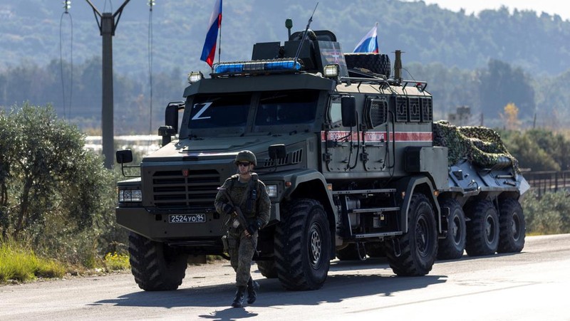 Seorang tentara Rusia berpatroli terhadap konvoi militer di pinggir jalan karena kerusakan mesin di salah satu kendaraan saat mereka melakukan perjalanan melalui pangkalan udara Hmeimim di wilayah pesisir Latakia, Suriah, 14 Desember 2024. (REUTERS/Umit Bektas)