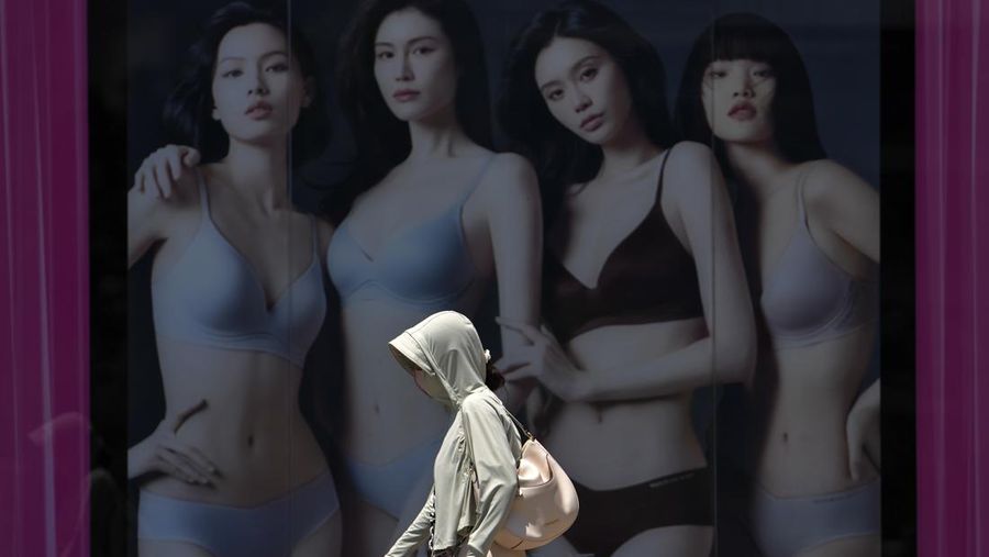 Seorang wanita yang mengenakan pakaian pelindung matahari berjalan melewati poster iklan pakaian dalam di luar pusat perbelanjaan pada hari yang panas dan cerah di Beijing, Senin, 24/6. (AP Photo/Andy Wong)