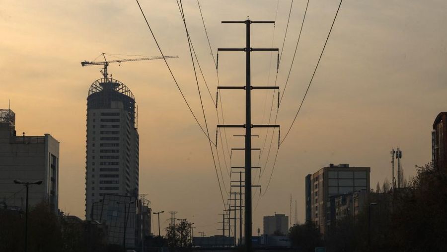 Arus lalu lintas di jalan utama melewati menara transmisi listrik di Teheran pada 16 Desember 2024. Iran telah menghentikan operasi di beberapa pembangkit listrik karena kekurangan bahan bakar yang diperparah oleh meningkatnya permintaan selama cuaca dingin. (Photo by ATTA KENARE / AFP)